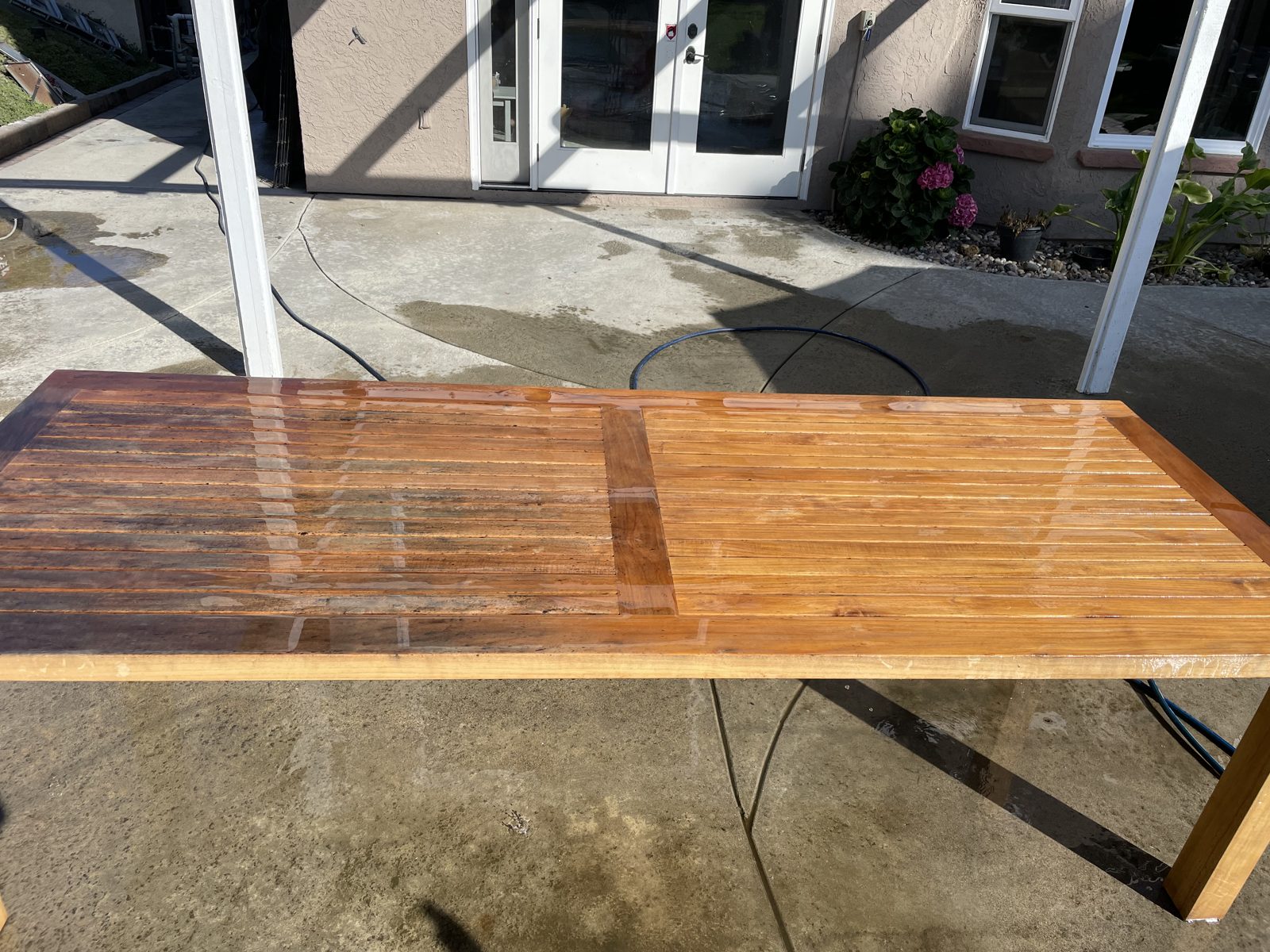 Teak outdoor table part-way through restoration, showing the restored half